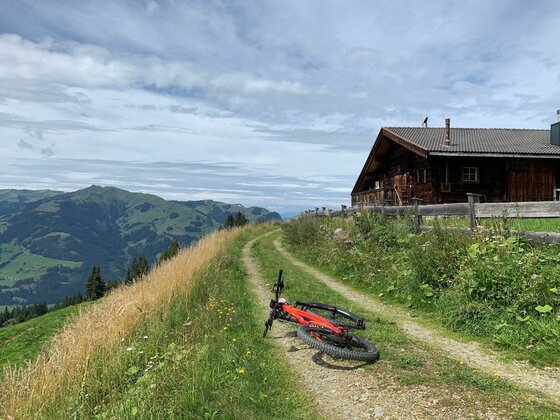 Mountainbike bei der Branderalm Ein rotes Mountainbike liegt auf einem Schotterweg neben einer Holzhütte vor Bergpanorama.