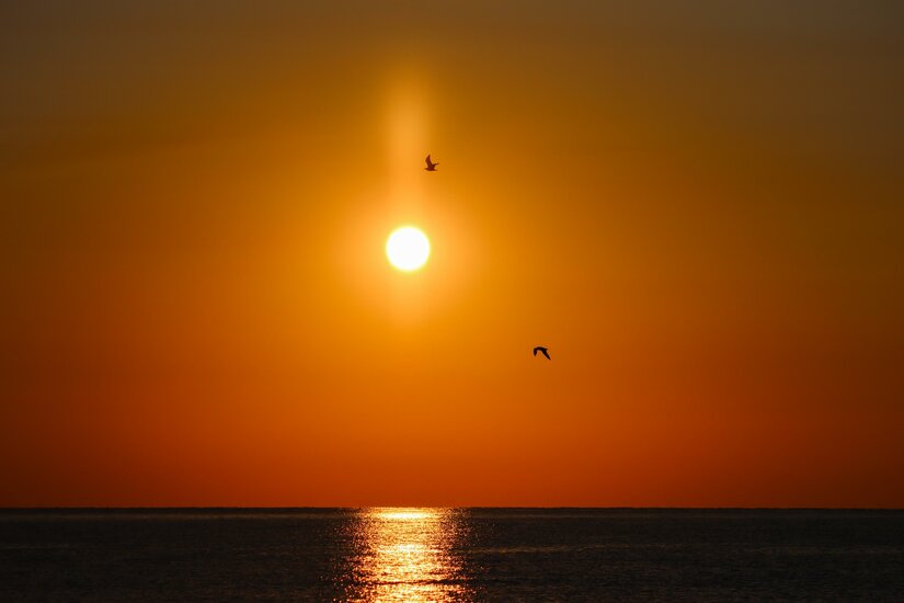 Ein schöner Sonnenuntergang über dem Wasser. Die orangefarbenen und goldenen Töne spiegeln sich im Meer.