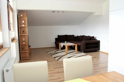 Wohnzimmer im Kitzbühel Apartment Wohnzimmer mit braunem Ecksofa, Holztisch auf Teppich und hellem Laminatboden unter einer Dachschräge.