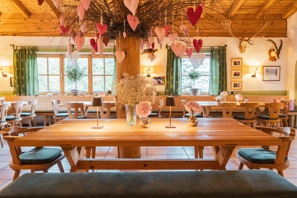 Ein gemütliches Restaurant mit Holztischen, dekoriert mit rosa Herzen und frischen Blumen in eleganten Vasen.