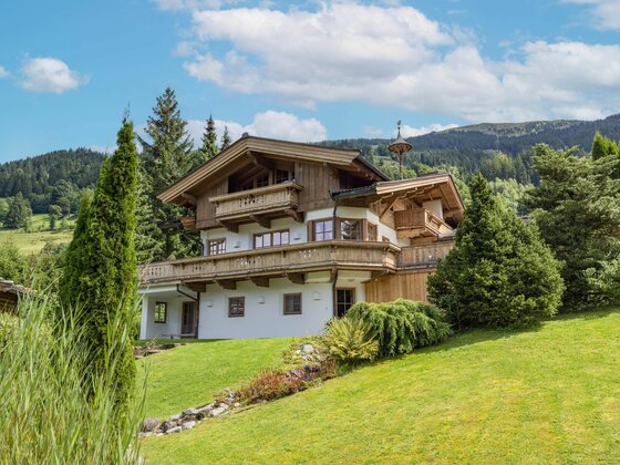 Haus Schmidt in Jochberg Mehrstöckiges Alpenhaus aus Holz und weißem Putz mit Balkonen auf einer grünen Wiese vor bewaldeten Bergen.