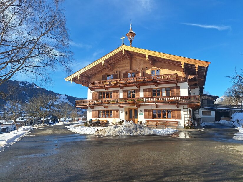 20260115_132644 Ein traditionelles Chalet im Winter, umgeben von Schnee. Der Himmel ist blau und die Landschaft ist malerisch.