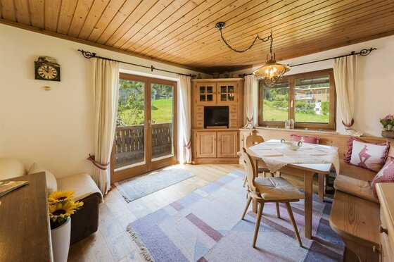 Landhaus Klotz App. Elke Rustikaler Wohnraum mit Holzdecke, Sitzecke, Esstisch und Balkonzugang.