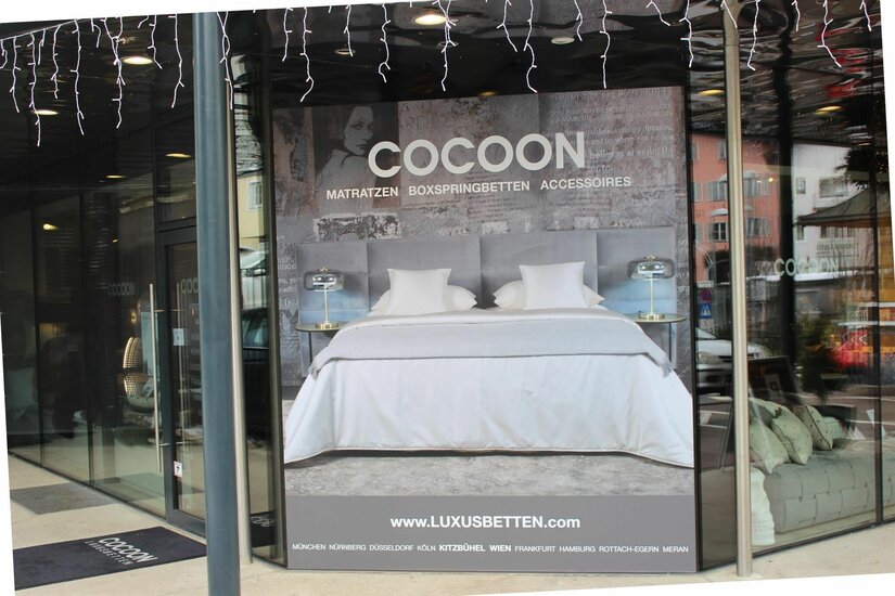 Cocoon Bettenfachgeschäft Schaufenster eines Bettengeschäfts mit großem Werbeplakat für Matratzen und Boxspringbetten.