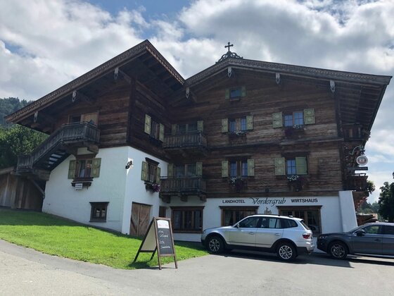 Landhotel Vordergrub Traditionelles Landhotel aus dunklem Holz mit weißen Fassadenelementen und parkenden Autos davor.