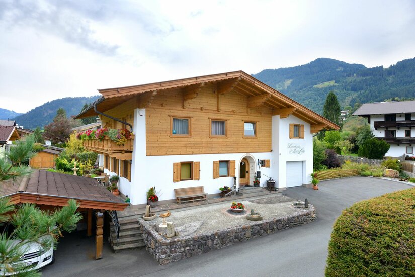 Landhaus Marie Luise Zweistöckiges Landhaus mit Holzfassade im Obergeschoss und Bergen im Hintergrund.
