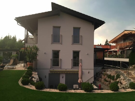 Hausansicht Appartement Lyso Modernes zweistöckiges Wohnhaus mit hellem Putz, dunklem Dach und gepflegtem Gartenbereich.