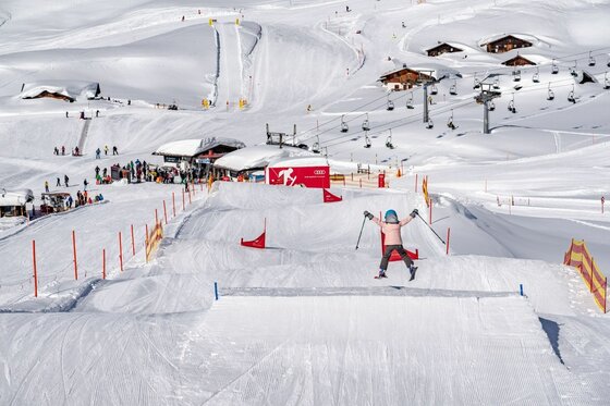 Snowpark am Kitzbüheler Horn Ein Kind springt auf Skiern über eine Schanze in einem Snowpark mit Sessellift im Hintergrund.