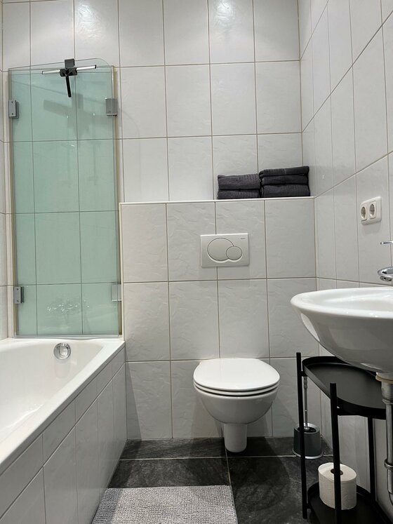 Ein modernes Badezimmer mit einer Badewanne und einer Dusche. Die Wände sind hell gefliest und es gibt frische Handtücher.