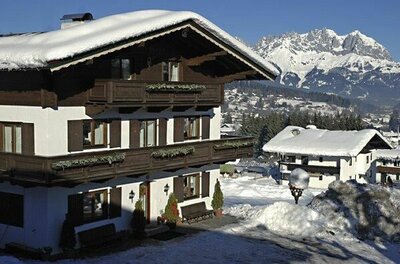 Pension Feiersinger im Winter Alpines Gästehaus mit Holzbalkonen und schneebedecktem Dach vor verschneitem Bergmassiv.