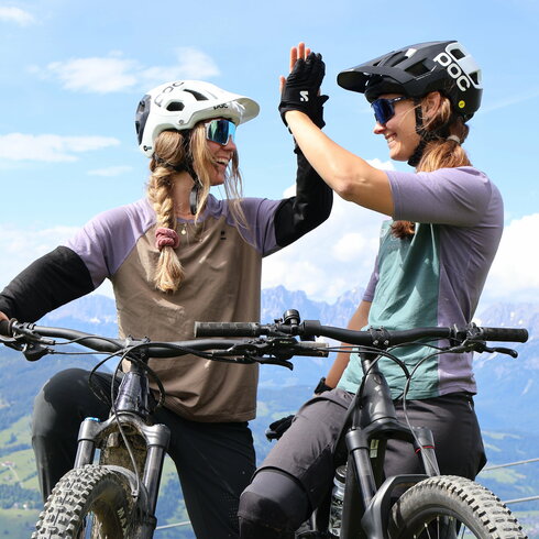 In Kitzbühel, two female mountain bikers high-five each other in a meadow and celebrate their success.