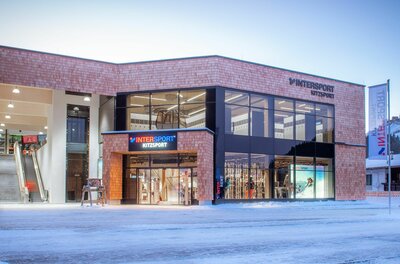 Intersport Kitzsport Fleckalmbahn Modernes Sportgeschäft mit Holzfassade und großen Glasfronten im Winter.