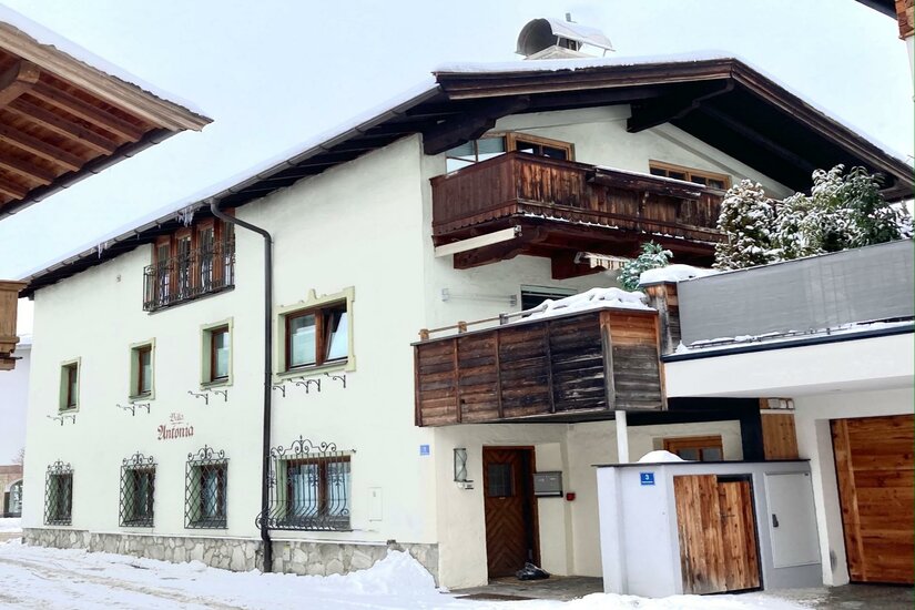 Belle Kitz Winter Außenansicht Zweistöckiges weißes Alpenhaus mit Holzbalkonen und schneebedecktem Dach im Winter.