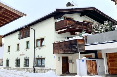 Belle Kitz Winter Außenansicht Zweistöckiges weißes Alpenhaus mit Holzbalkonen und schneebedecktem Dach im Winter.