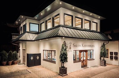 Beleuchtete Außenansicht des zweistöckigen Gebäudes Salon Kaiserblick bei Nacht.