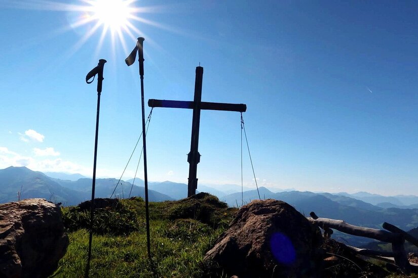 Gipfelkreuz Horn Südberge Gipfelkreuz und Wanderstöcke vor Gebirgspanorama bei Sonnenschein.