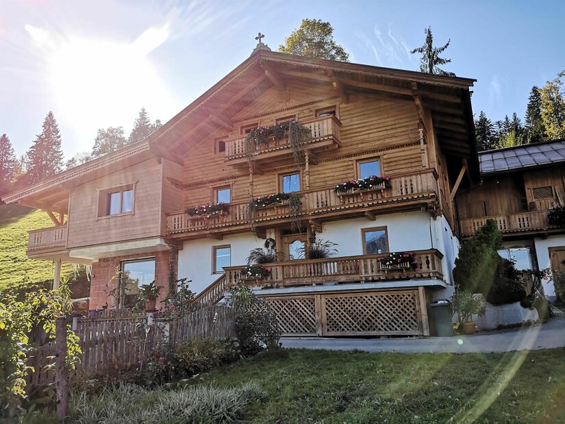 Alpiner Brandhof Mehrstöckiges Holzhaus im alpinen Stil mit Blumenbalkonen und weißem Erdgeschoss unter blauem Himmel.