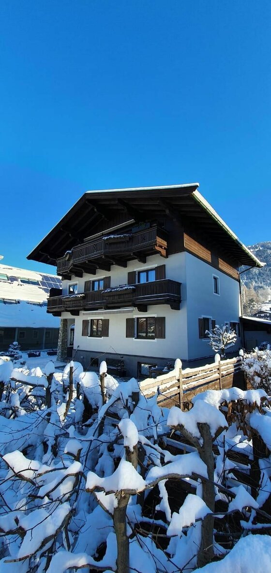 Mehrstöckiges alpines Wohnhaus mit Holzbalkonen im Winter vor blauem Himmel.