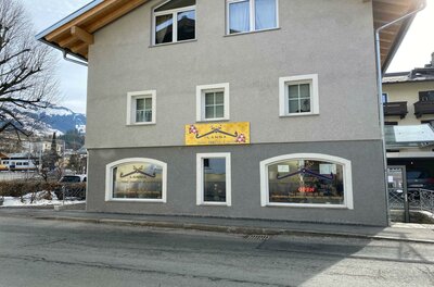 Ein modernes Gebäude mit grau gestrichener Fassade und großen Fenstern. An der Wand ist ein leuchtendes Schild angebracht, das Aufmerksamkeit erregt.