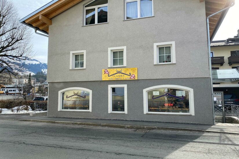 Lanna Thai Imbiss Ein modernes Gebäude mit grau gestrichener Fassade und großen Fenstern. An der Wand ist ein leuchtendes Schild angebracht, das Aufmerksamkeit erregt.