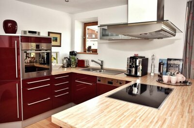 Moderne Einbauküche mit weinroten Fronten, Holz-Arbeitsplatte, Induktionskochfeld und Kaffeemaschine.