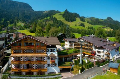 Hotel Kaiserhof Kitzbühel im Sommer Mehrstöckiges Hotelgebäude in alpiner Bauweise mit Holzfassade und Seilbahnstation im Vordergrund.