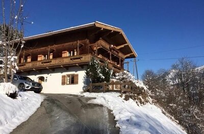 Zweistöckiges Holzhaus mit weißem Erdgeschoss in verschneiter Berglandschaft unter blauem Himmel.
