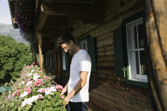 A man stands in front of a hut with flowers
