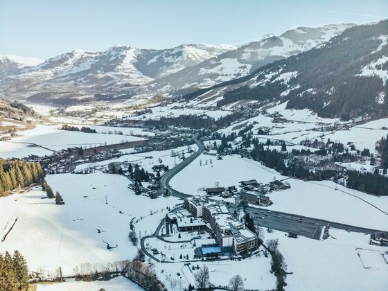 Kempinski Hotel Das Tirol Winteransicht Luftaufnahme eines Hotels in einer verschneiten Gebirgslandschaft mit umliegenden Wäldern und Straßen.