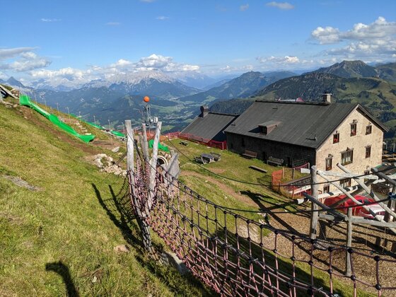 Berghütte am Kitzbüheler Horn Steinerne Berghütte mit Spielplatz und Rutsche am Grashang vor Gebirgspanorama.