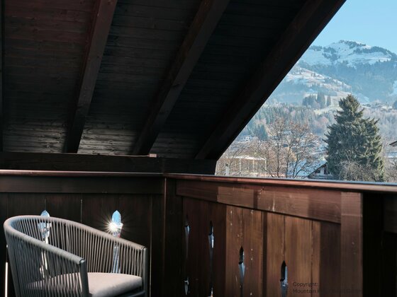 Holzbalkon mit modernem Sessel und Blick auf schneebedeckte Berge.