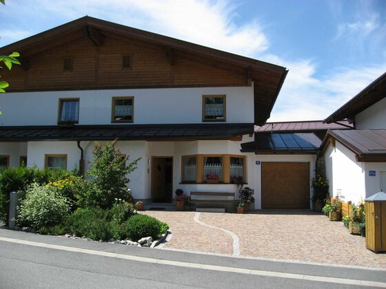 Vorderansicht eines zweistöckigen Wohnhauses mit weißer Fassade, Holzgiebel und gepflasterter Einfahrt.