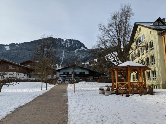 Verschneiter Weg im Ort mit Holzpavillon, Gebäuden und bewaldetem Berg im Hintergrund.