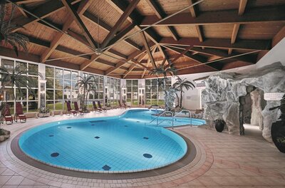 Wellnessbereich Lisi Family Hotel Hallenbad mit Holzdecke, Palmen, Liegestühlen und einer künstlichen Felsengrotte.