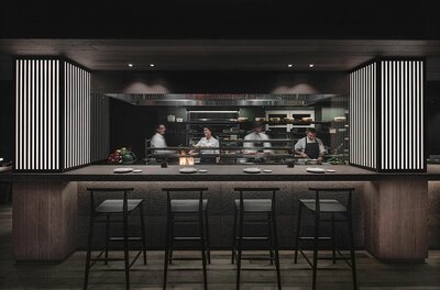 Restaurant ZUMA Innenansicht Blick auf eine offene Restaurantküche mit Köchen hinter einem Tresen mit Barhockern.