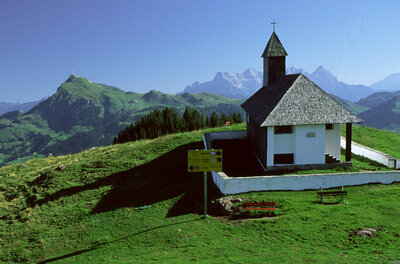 St. Bernhard Kapelle am Berg Kleine Kapelle mit Schindeldach auf einem grünen Bergrücken vor alpinem Panorama.
