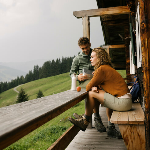 Entspannte Atmosphäre bei der Wanderpause in den Bergen Zwei Personen sitzen vor einer Berghütte.