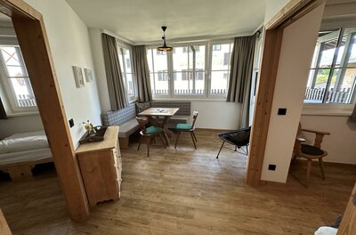 Eine helle und einladende Wohnung mit Holzböden und großen Fenstern. Der Essbereich ist mit einem Tisch und bunten Stühlen ausgestattet.