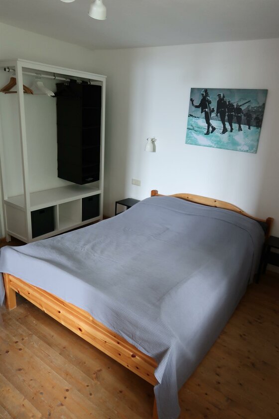 Kitzbühel Retro Apartment Schlafzimmer Schlafzimmer mit Holzbett, grauem Überwurf, offenem Kleiderschrank und einem Bild von Skifahrern an der Wand.