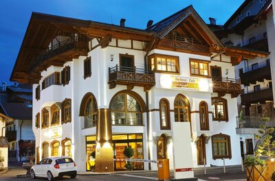 Beleuchtetes Gebäude der Bäckerei Schmidt bei Dämmerung mit weißer Fassade und Holzbalkonen.