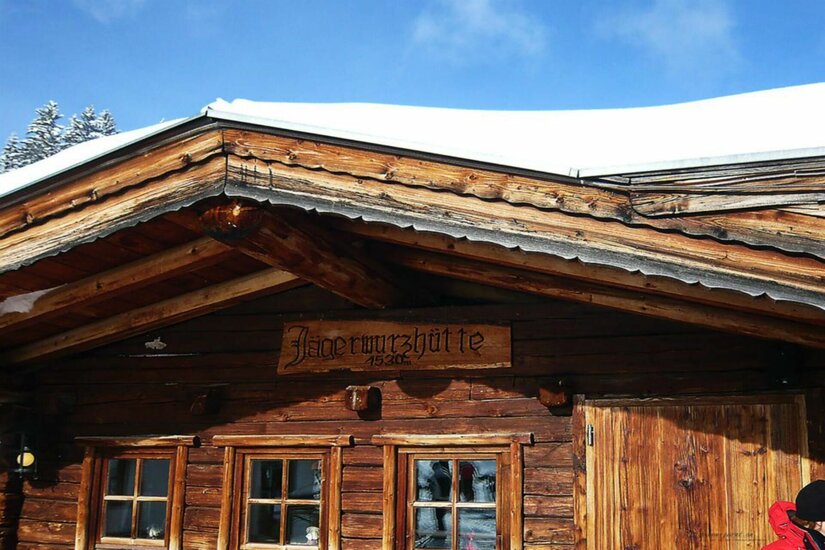 Jagerwurzhütte im Winter Holzfassade der Jagerwurzhütte mit Namensschild und schneebedecktem Dach unter blauem Himmel.
