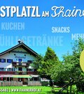 Außenansicht des Thainerhofs mit Terrasse, Sonnenschirmen und umliegenden Bäumen unter blauem Himmel.