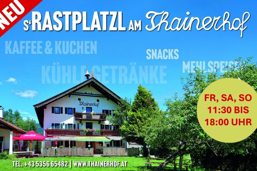 Außenansicht des Thainerhofs mit Terrasse, Sonnenschirmen und umliegenden Bäumen unter blauem Himmel.