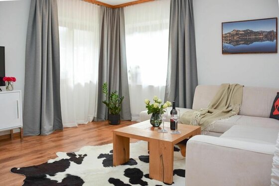 Wohnzimmer mit hellem Sofa, Holztisch, Kuhfellteppich und grauen Vorhängen.