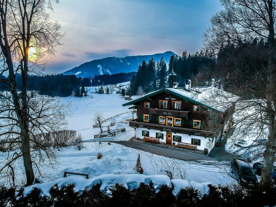 Hof Oberhaus im Winter Ein traditionelles Holzhaus in einer verschneiten Berglandschaft bei Sonnenuntergang.
