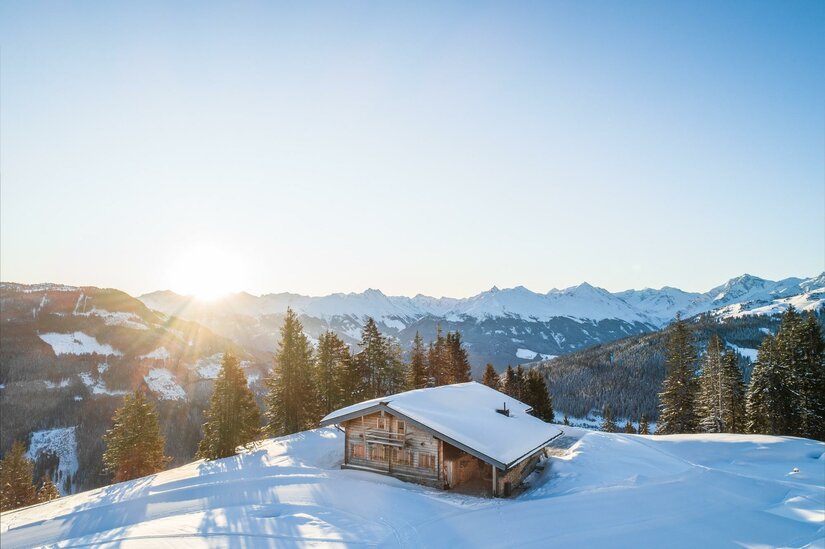 Wirts Hochalm im Winter Holzhütte in verschneiter Berglandschaft bei Sonnenaufgang.