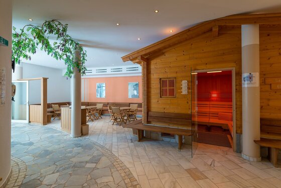 Sauna 2 Eine gemütliche Saunalandschaft mit einer Holzsauna und einem hellen, einladenden Raum. Der Boden ist mit hellen Steinen gefliest und Pflanzen sorgen für eine entspannte Atmosphäre.
