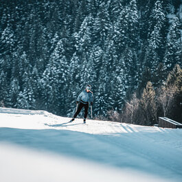 During a cross-country skiing event in Kitzbühel, a skier glides gracefully along a snow-covered trail with fir trees in the background.
