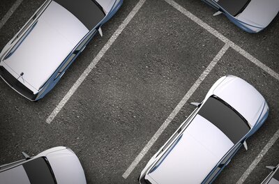 Parkplatz aus der Vogelperspektive Vogelperspektive auf einen asphaltierten Parkplatz mit weißen Markierungen und mehreren geparkten Autos.