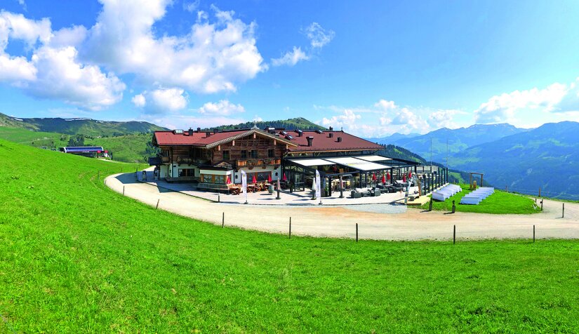 Sonnalm Sommer Ein gemütliches Berghaus umgeben von grünen Wiesen und Bergen. Der Himmel ist klar mit einigen Wolken.